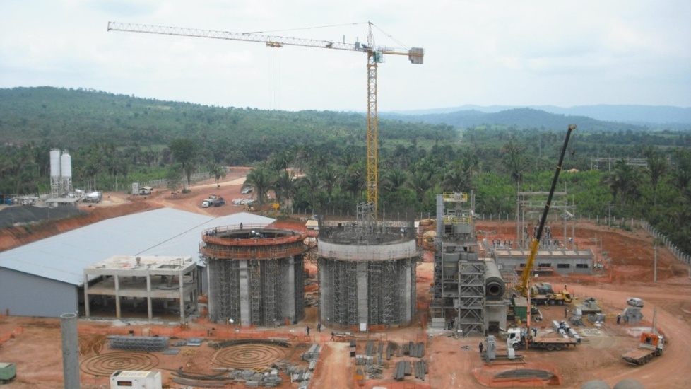 Obras en construcción de una planta industrial en zona selvática, con grúas y estructuras cilíndricas en proceso